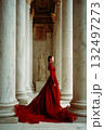 A woman in a red dress stands in front of a marble pillar 132497273