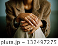 A woman is sitting with her hands on her lap, wearing a ring on her left hand 132497275
