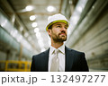 A man in a suit and a yellow hard hat stands in a large, empty building 132497277
