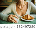 A woman is sitting at a table with a croissant and a stack of bills 132497280