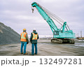 Two men are standing next to a large green crane 132497281