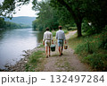 Two people walking along a path by a river, one of them holding a green cooler 132497284