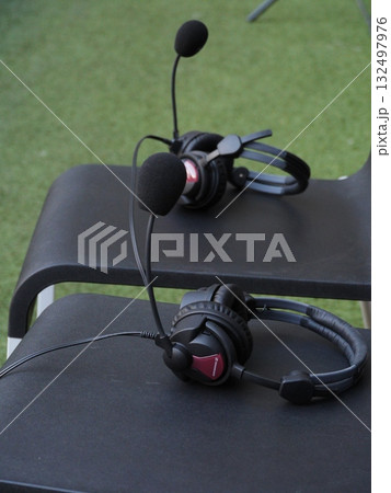 Two black headphones with microphones on them sit on a black chair 132497976