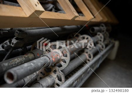 Stack of metal scaffolding parts stored with wooden planks above creates industrial composition. Scratched steel surfaces show signs of use and construction work preparation Stack of metal scaffolding parts stored with wooden planks above creates industrial composition. Scratched steel surfaces show signs of use and construction work preparation 132498180