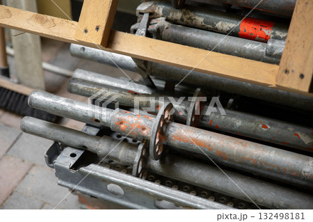 Stack of metal scaffolding parts stored with wooden planks above creates industrial composition. Scratched steel surfaces show signs of use and construction work preparation Stack of metal scaffolding parts stored with wooden planks above creates industrial composition. Scratched steel surfaces show signs of use and construction work preparation 132498181
