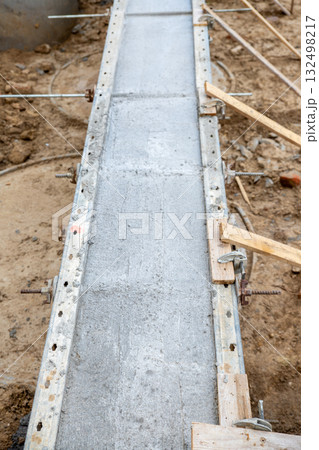 Concrete foundation poured into metal formwork at construction site. Steel rods, braces and rebar elements create strong structure supported by soil and wooden beams 132498217