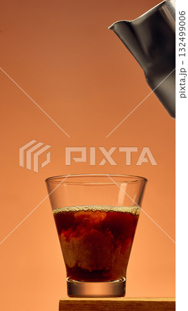 Coffee in glass with rich swirl texture and metal pitcher above against warm background Coffee in glass with rich swirl texture and metal pitcher above against warm background 132499006