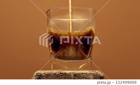 Espresso stream pouring into glass with foam forming on top against warm brown background Espresso stream pouring into glass with foam forming on top against warm brown background 132499009
