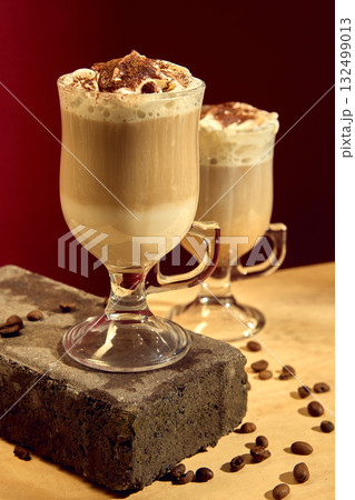 Latte with whipped cream and cocoa powder topping in glass cup with roasted coffee beans 132499013