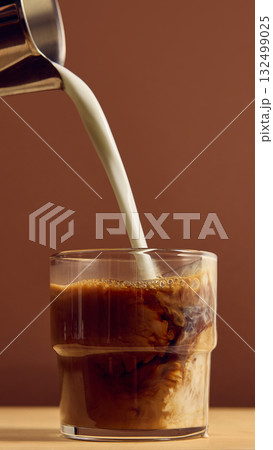 Milk stream mixing with dark espresso in glass closeup showing creamy swirl and contrast 132499025