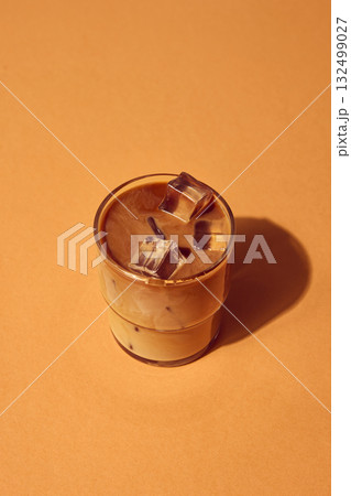 Iced coffee with milk and ice cubes in glass on warm beige background under natural light 132499027