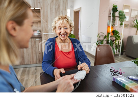 Cheerful interaction between caregiver and elderly woman in bright living space 132501522