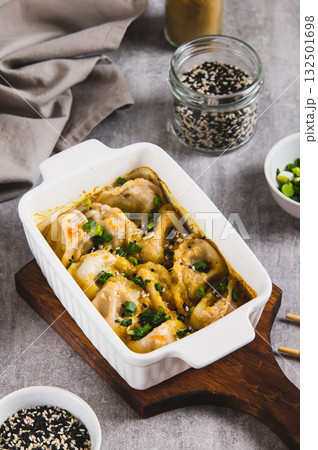 Dumpling Bake in coconut curry sauce with sesame seeds in a baking dish vertical view 132501698