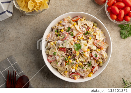 Homemade macaroni salad with bow tie pasta and canned tuna, carrot, onion, corn, tomato, green peas and mayonnaise dressing in a white plate on wooden table.Top view. Homemade macaroni salad with bow tie pasta and canned tuna, carrot, onion, corn, tomato, green peas and mayonnaise dressing in a white plate on wooden table.Top view. 132501871