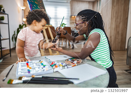 Mom teaches child to paint on a sunny afternoon indoors Mom teaches child to paint on a sunny afternoon indoors 132501997