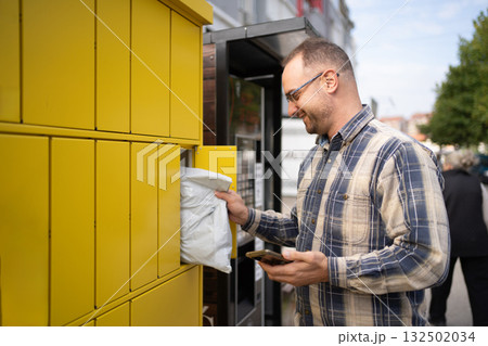 Man retrieves package from bright yellow delivery locker in urban setting on a sunny day Man retrieves package from bright yellow delivery locker in urban setting on a sunny day 132502034