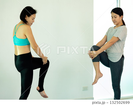 Two middle-aged Asian women practicing yoga or stretching together in a bright indoor space. Healthy lifestyle, mindfulness, and fitness concept for wellness, aging well, and mental balance 132502699