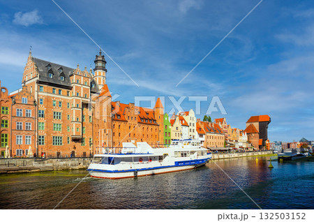 Scenic view of two boats navigating the Motlawa River alongside historic colorful buildings in Gdansk, Poland. Bright blue skies enhance this vibrant European cityscape 132503152