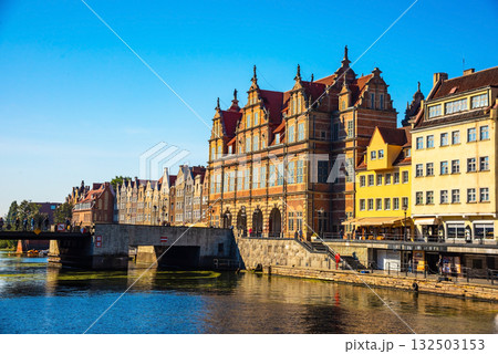 Scenic view of historic architecture and a bridge over a calm river in Gdansk, Poland. Bright day showcases ancient buildings reflecting in the water, offering cultural and travel allure. Scenic view of historic architecture and a bridge over a calm river in Gdansk, Poland. Bright day showcases ancient buildings reflecting in the water, offering cultural and travel allure. 132503153