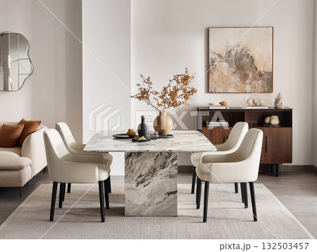 A chic, minimalist dining room featuring a round concrete table, white boucle chairs, an arched mirror, and dried floral arrangements against a neutral wall. A chic, minimalist dining room featuring a round concrete table, white boucle chairs, an arched mirror, and dried floral arrangements against a neutral wall. 132503457