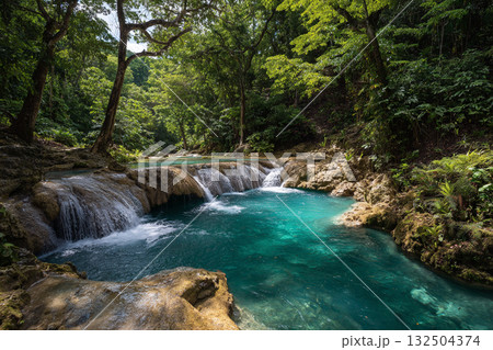 A stunning jungle waterfall cascades into a vibrant turquoise pool surrounded by lush green foliage and large brown rocks, creating a secluded natural oasis. A stunning jungle waterfall cascades into a vibrant turquoise pool surrounded by lush green foliage and large brown rocks, creating a secluded natural oasis. 132504374