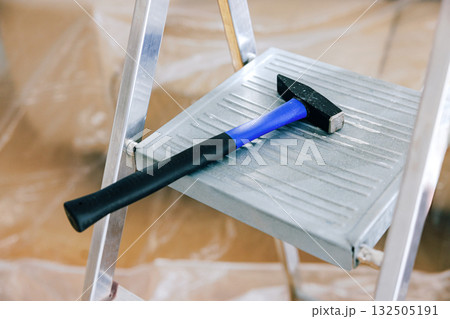 Black and blue hammer resting on aluminum step ladder in a construction 132505191