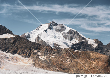 Piz Bernina towers in the Swiss Alps, showcasing its majestic glacier-covered summit against a clear blue sky. The rugged terrain and stunning natural beauty draw visitors year-round. 132506270