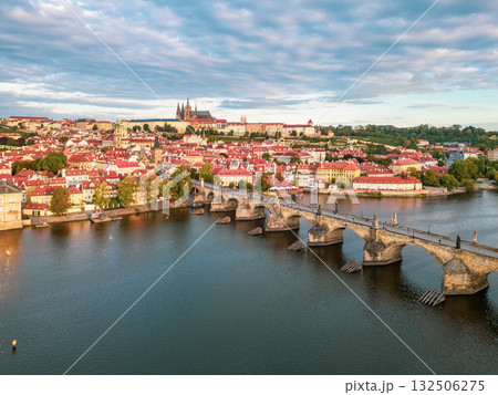 Early morning light casts a warm glow over Prague Castle and Charles Bridge. The Vltava River reflects the stunning architecture and the surrounding old town buildings. 132506275