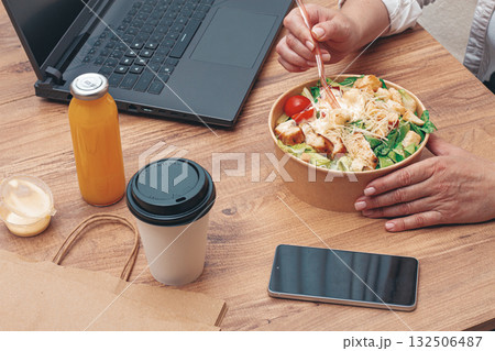 a woman is working on a laptop at home, there is food on the table, salad, coffee and juice, delivery, 132506487