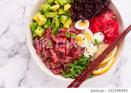 Fresh poke bowl, with tuna, avocado, and vegetables, served on a white plate Fresh poke bowl, with tuna, avocado, and vegetables, served on a white plate 132506493
