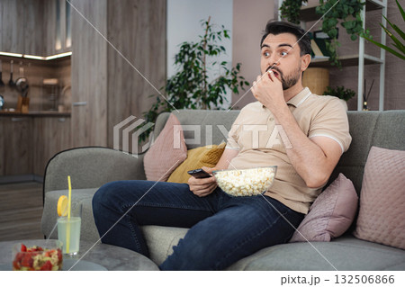 Man watching tv and eating popcorn on the sofa at home Man watching tv and eating popcorn on the sofa at home 132506866