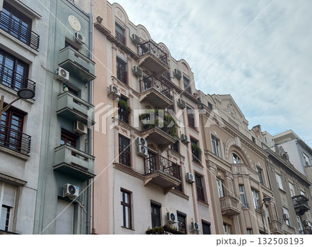 Historic residential architecture with balconies and air conditioners under cloudy sky. Urban texture, lifestyle, and heritage building facade in European city. 132508193