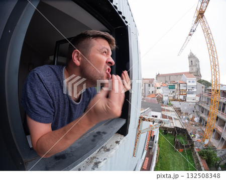 Man angrily staring at a noisy construction site outside his apartment window Man angrily staring at a noisy construction site outside his apartment window 132508348