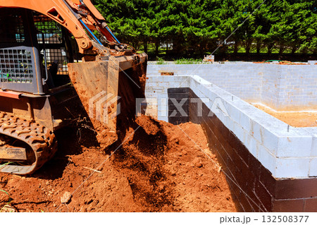 Construction worker operates excavator to load soil into building foundation 132508377