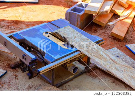 Circular saw is cutting through piece of plywood at busy construction site surrounded by wooden materials. Circular saw is cutting through piece of plywood at busy construction site surrounded by wooden materials. 132508383