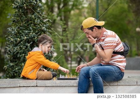 Boy with father playing chess outdoor. Learning strategic game. Education. Boy with father playing chess outdoor. Learning strategic game. Education. 132508385