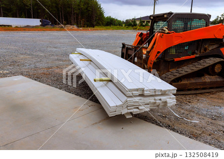 Stacked lumber rests on flat surface beside compact track loader at construction site 132508419