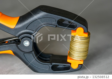 Stack of coins squeezed in black and orange clamp symbolizing economic pressure and inflation 132508512