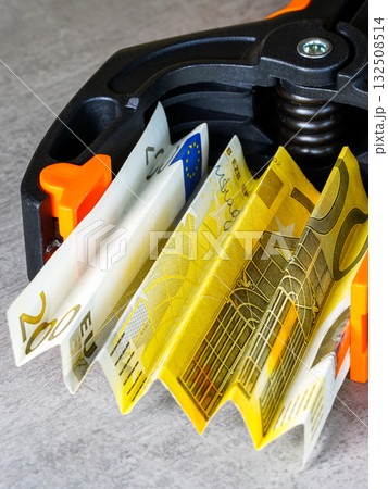 Euro banknotes squeezed in black and orange clamp symbolizing financial stress and inflation crisis Euro banknotes squeezed in black and orange clamp symbolizing financial stress and inflation crisis 132508514
