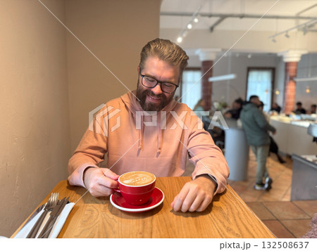 Man enjoying latte in modern cafe. Everyday relaxation, morning ritual and cozy coffee culture in urban lifestyle setting. 132508637