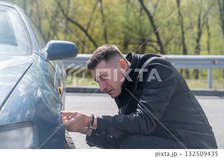 A Caucasian man inspects damage to his car. A Caucasian man inspects damage to his car. 132509435