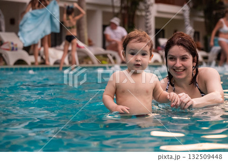 Caucasian woman holds her son while swimming in a pool on vacation. Mom teaches little boy to swim. Caucasian woman holds her son while swimming in a pool on vacation. Mom teaches little boy to swim. 132509448