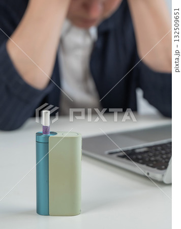 Tired businesswoman smoking an electronic cigarette while working on a laptop. Tobacco heating system. 132509651