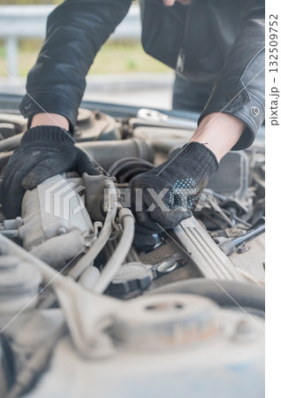 A man changes spark plugs in his car. A man changes spark plugs in his car. 132509752