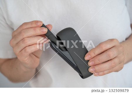 A woman takes a tobacco heating system out of a charger. Electronic cigarette. A woman takes a tobacco heating system out of a charger. Electronic cigarette. 132509879
