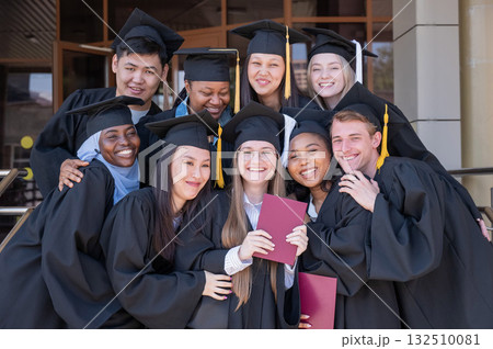 Happy students of different nationalities in graduation gowns hold their diplomas. Happy students of different nationalities in graduation gowns hold their diplomas. 132510081
