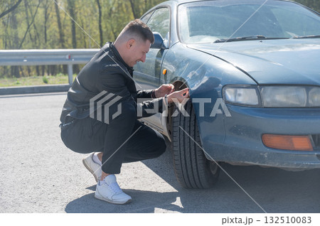 Caucasian man examines and tries to fix a deformation on the body of his car.  132510083