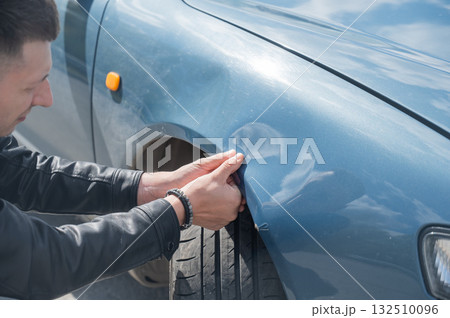 Caucasian man examines and tries to fix a deformation on the body of his car.  132510096