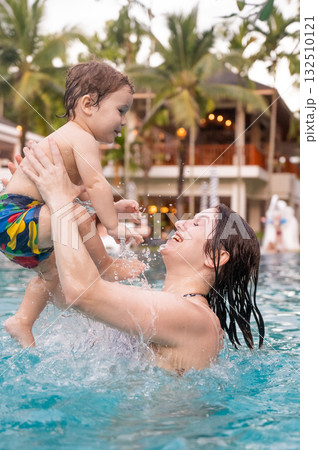 Caucasian woman holds her son while swimming in a pool on vacation. Mom teaches little boy to swim. Caucasian woman holds her son while swimming in a pool on vacation. Mom teaches little boy to swim. 132510121