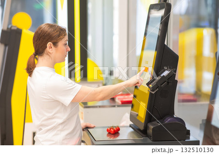 A woman weighs cherry tomatoes at a self-service checkout.  132510130